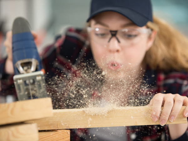 Kvinnlig snickare som blåser bort trädamm från det hon tillverkar